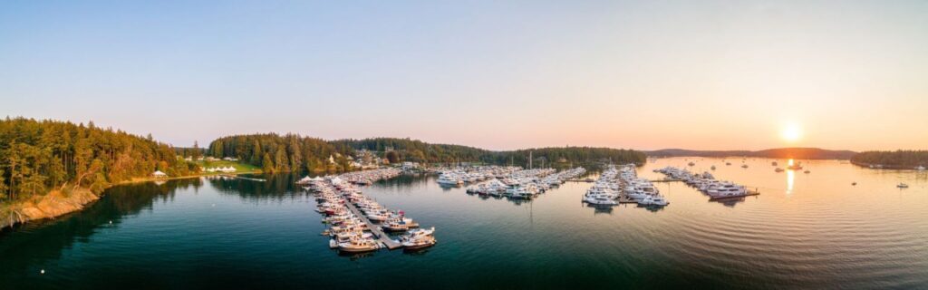 Wide-angle view of Roche Harbor Marina on San Juan Island at sunset, showcasing boats docked in calm waters with a colorful sky reflecting on the surface.